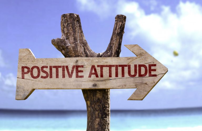 Wooden sign showing positive attitude with a beach background.