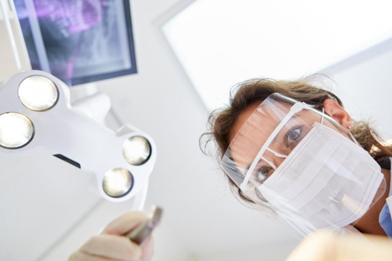 Young dentist with surgical mask and visor during a treatment or dental surgery in the dental clinic